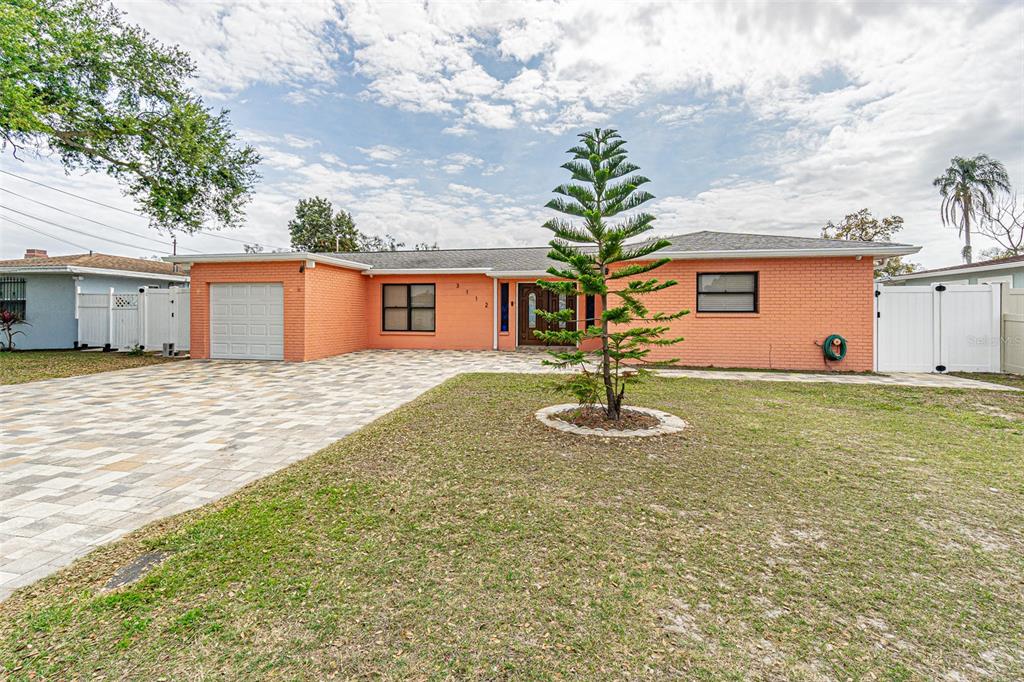 A single-story orange brick house features a paved driveway, a front lawn, and a pine tree — 3112 W HENRY AVENUE, TAMPA, FL