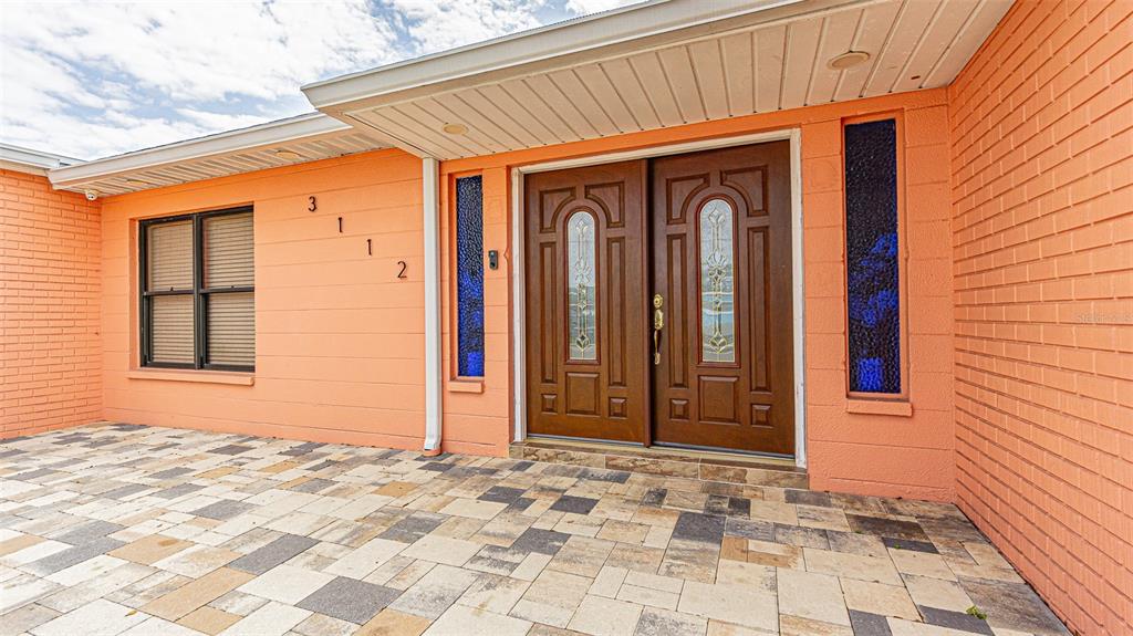 A peach-colored brick house exterior features a double front door and a paved patio — 3112 W HENRY AVENUE, TAMPA, FL