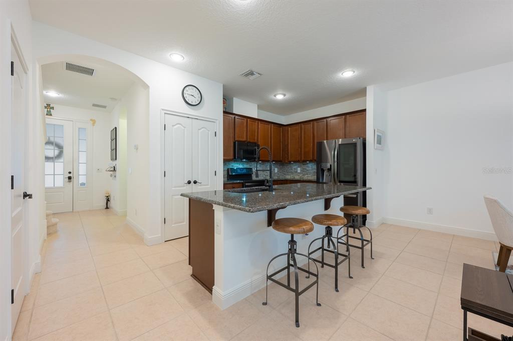 A kitchen features dark wood cabinets, granite countertops, a center island with stools, and tile flooring — 12305 VIA DERNA PLACE, WINDERMERE, FL