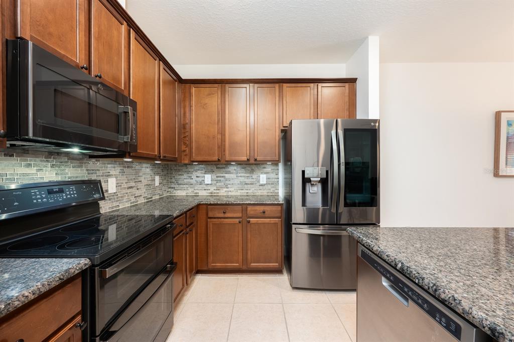 A kitchen features wood cabinets, granite countertops, stainless steel appliances, and a tiled backsplash — 12305 VIA DERNA PLACE, WINDERMERE, FL
