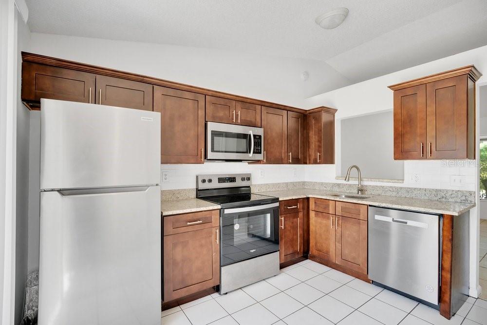 A kitchen features dark wood cabinets, stainless steel appliances, granite countertops, and white tile flooring — 2827 CORAL REEF DRIVE, ORLANDO, FL