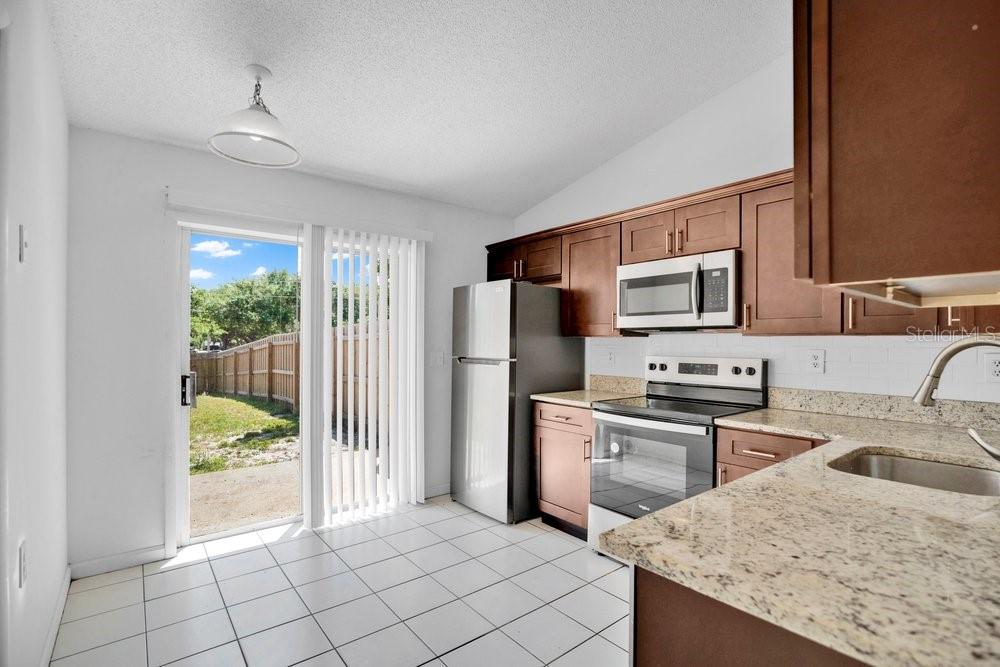 A kitchen with dark wood cabinets, granite countertops, stainless steel appliances, and a sliding glass door — 2827 CORAL REEF DRIVE, ORLANDO, FL