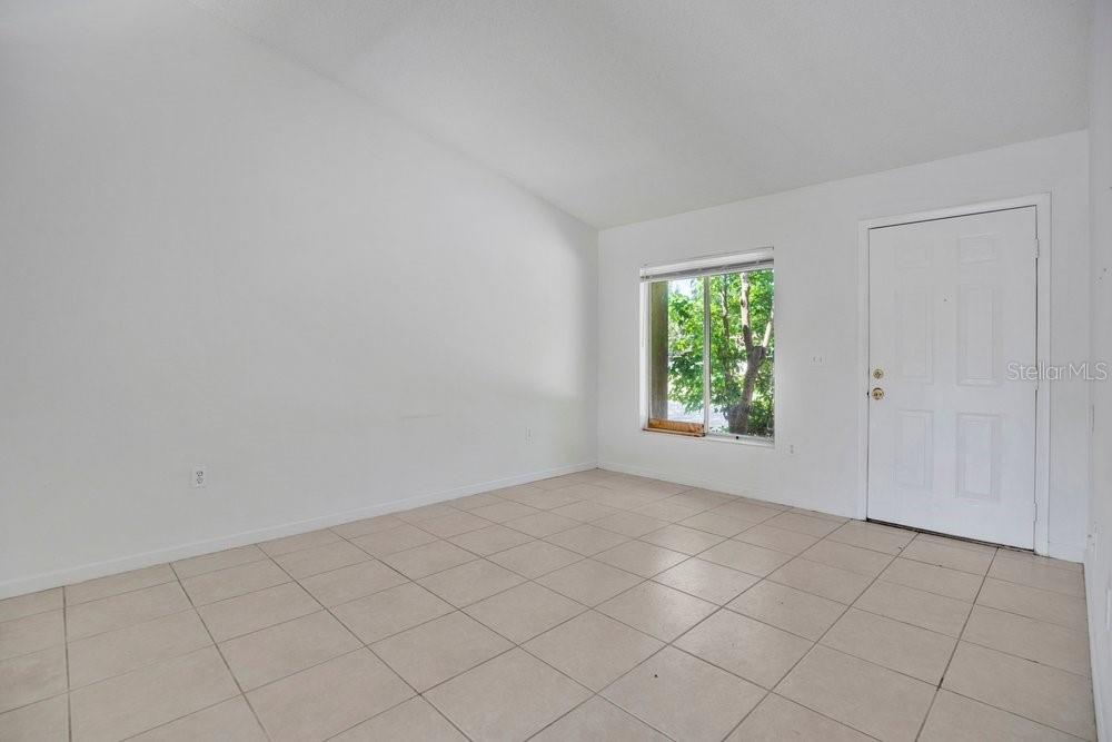 An empty room with white walls, light tile flooring, a window, and a white door — 2827 CORAL REEF DRIVE, ORLANDO, FL