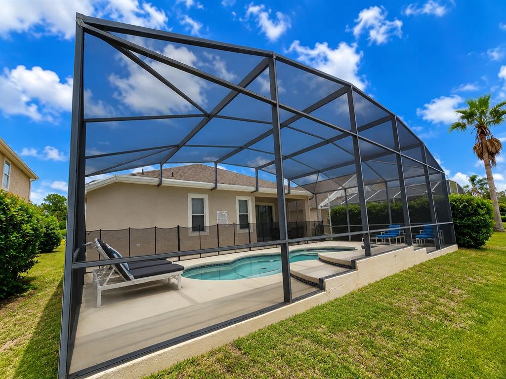 A swimming pool with a screen enclosure sits in a backyard next to a house — 205 GLENEAGLES DRIVE, DAVENPORT, FL