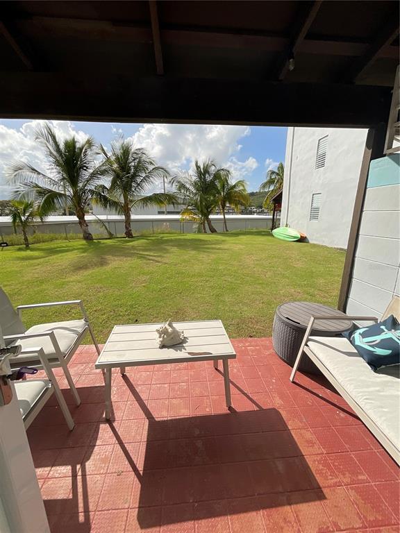 A covered patio with red tile flooring overlooks a grassy lawn with palm trees — Villa Marina Village APT 5 B, FAJARDO, PR
