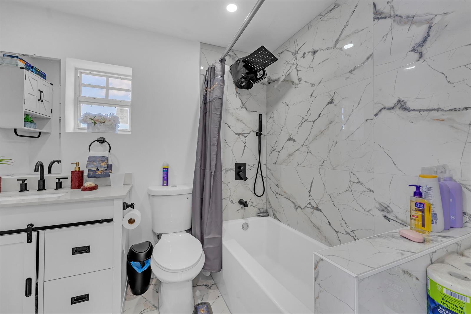 A bathroom features a white vanity, a toilet, and a bathtub with marble-patterned tile walls — 621 NW 15th Avenue, Pompano Beach FL 33069, POMPANO BEACH, FL