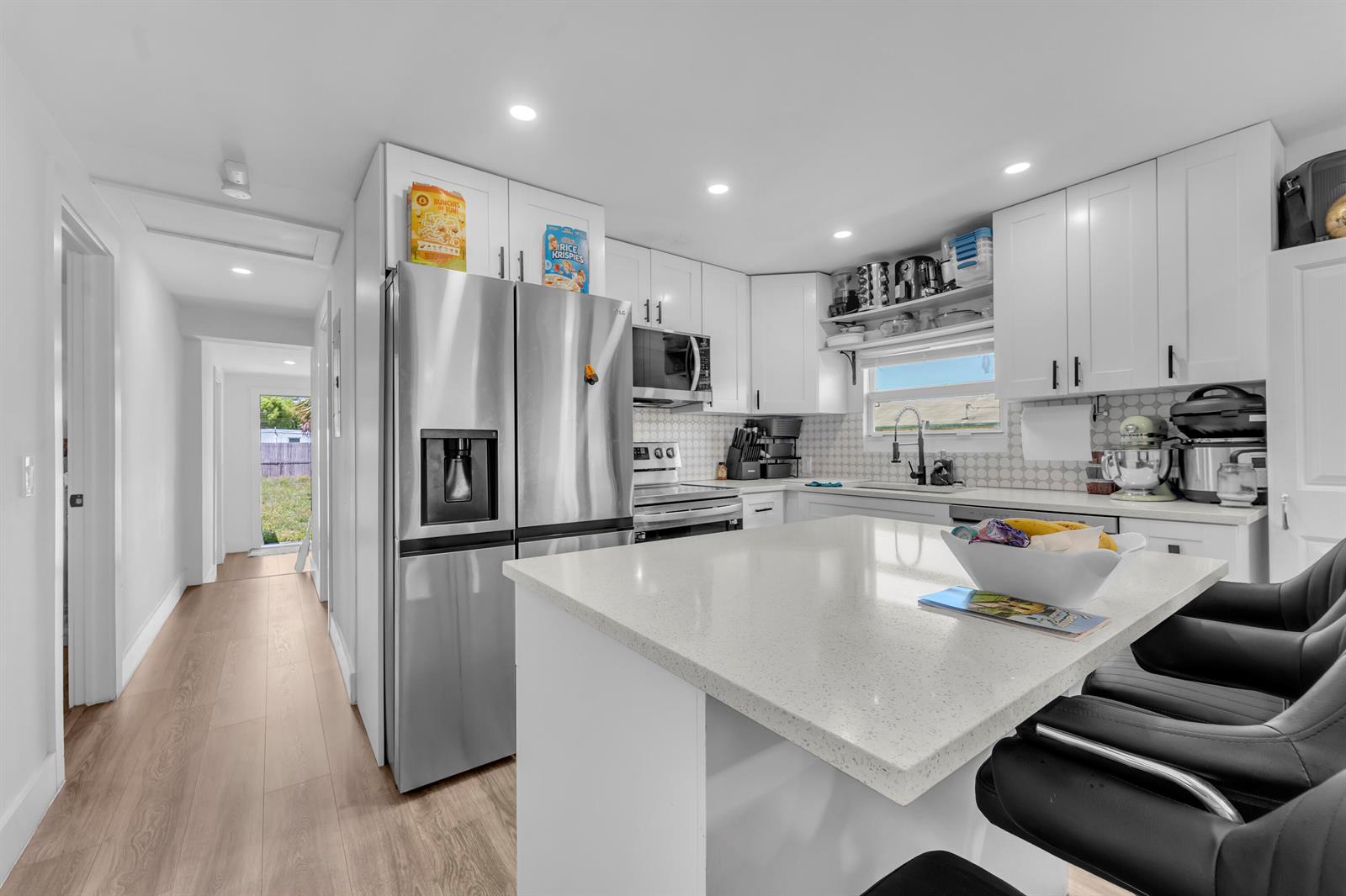A bright kitchen features white cabinetry, stainless steel appliances, and a quartz-topped island with seating — 621 NW 15th Avenue, Pompano Beach FL 33069, POMPANO BEACH, FL