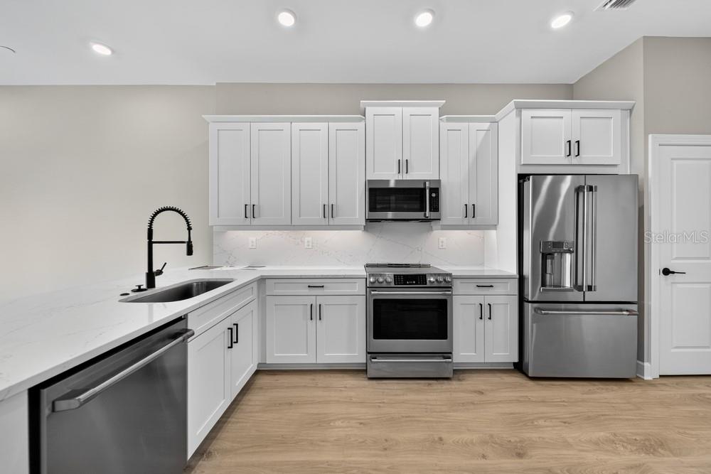 A modern kitchen features white cabinets, stainless steel appliances, and light wood-look flooring — 1617 SEA HAVEN DRIVE UNIT 504, PUNTA GORDA, FL