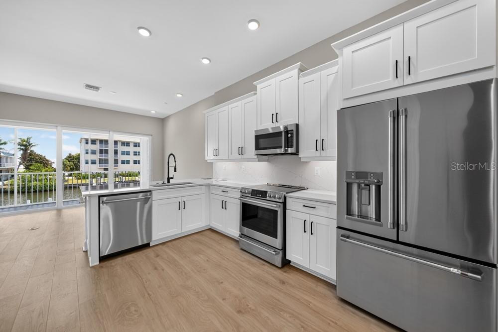 A modern kitchen features white cabinetry, stainless steel appliances, and light wood flooring — 1617 SEA HAVEN DRIVE UNIT 504, PUNTA GORDA, FL