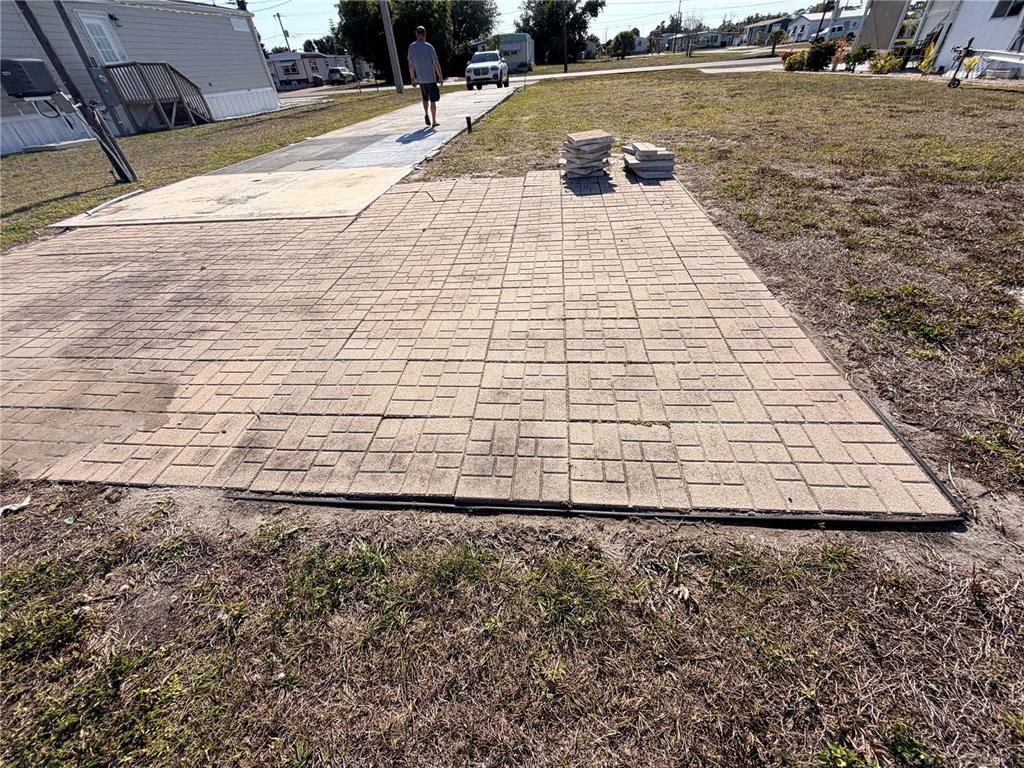 A paved patio area sits adjacent to a mobile home with a person walking nearby — 1387 FLAMINGO DRIVE, ENGLEWOOD, FL