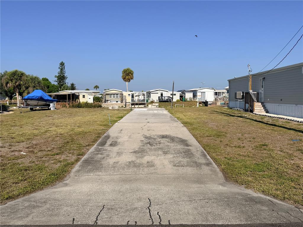 A concrete driveway leads toward a vacant lot surrounded by mobile homes and a boat — 1387 FLAMINGO DRIVE, ENGLEWOOD, FL