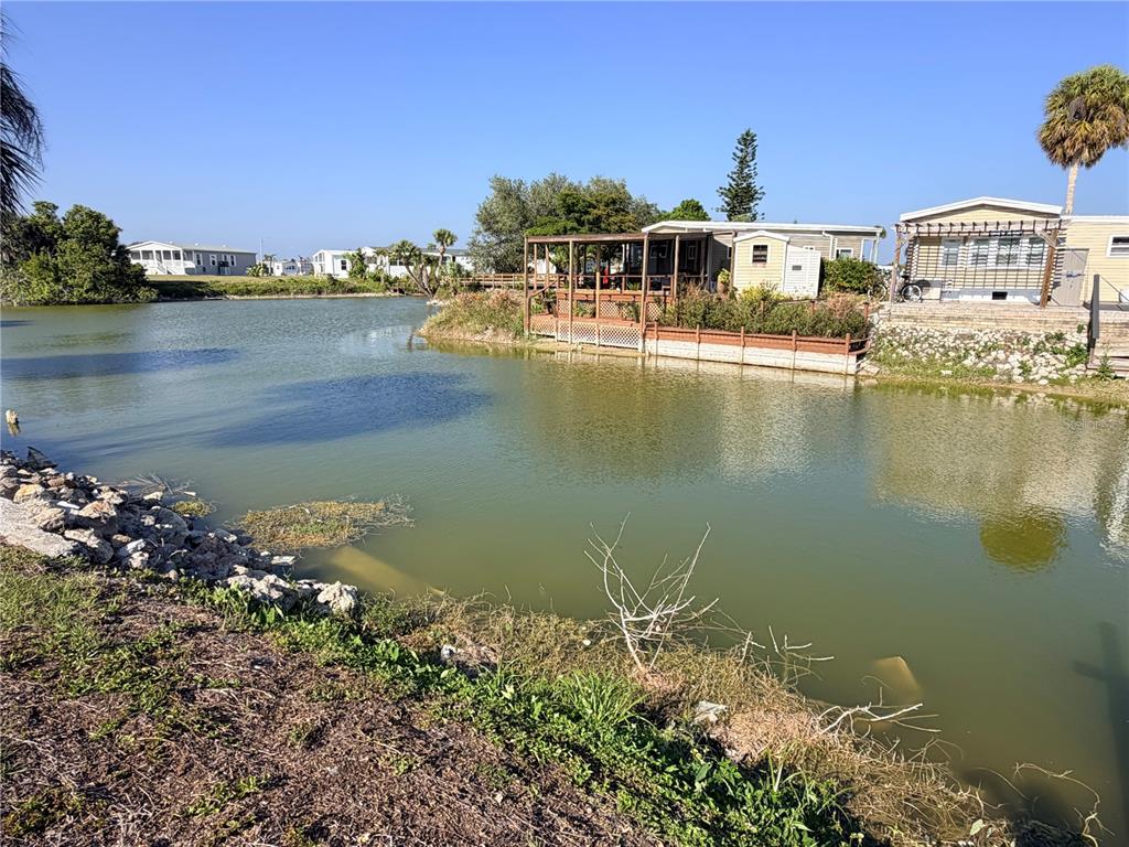 A pond sits in front of a mobile home with a wooden deck and pergola — 1387 FLAMINGO DRIVE, ENGLEWOOD, FL