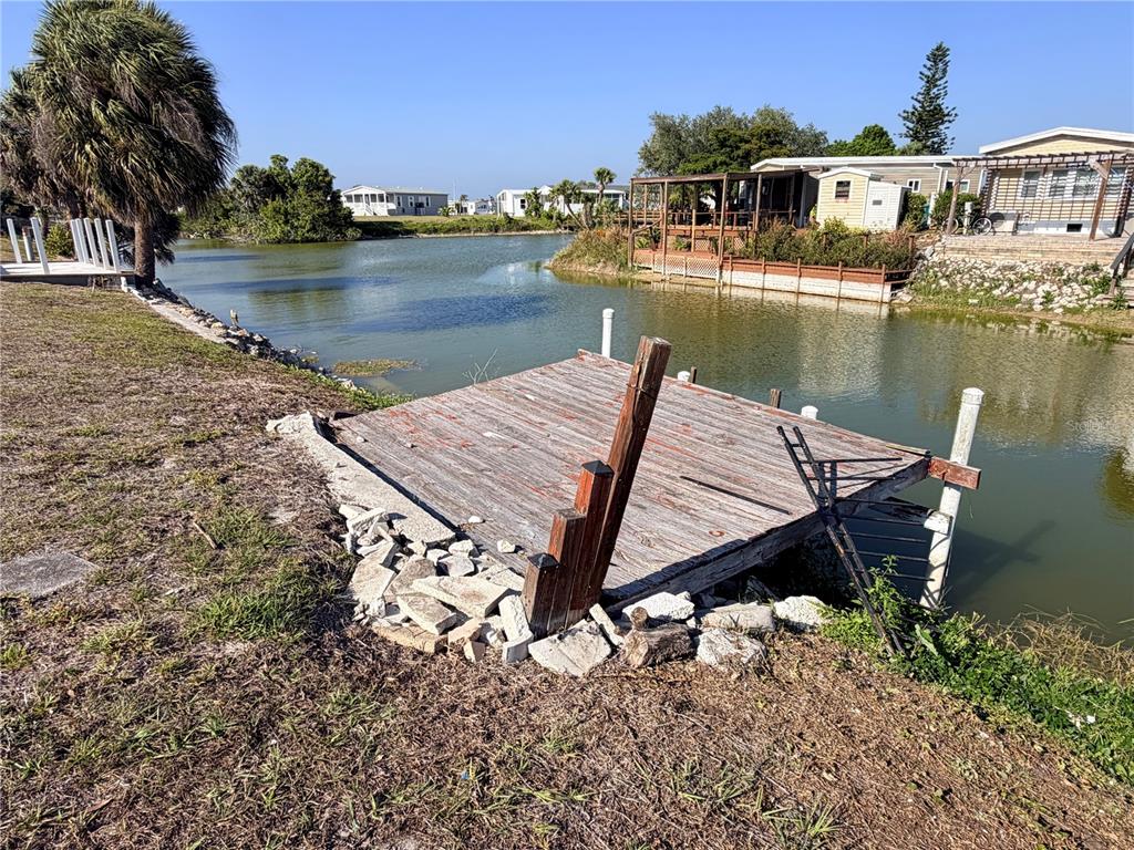 A weathered wooden dock sits on a grassy bank next to a small canal — 1387 FLAMINGO DRIVE, ENGLEWOOD, FL