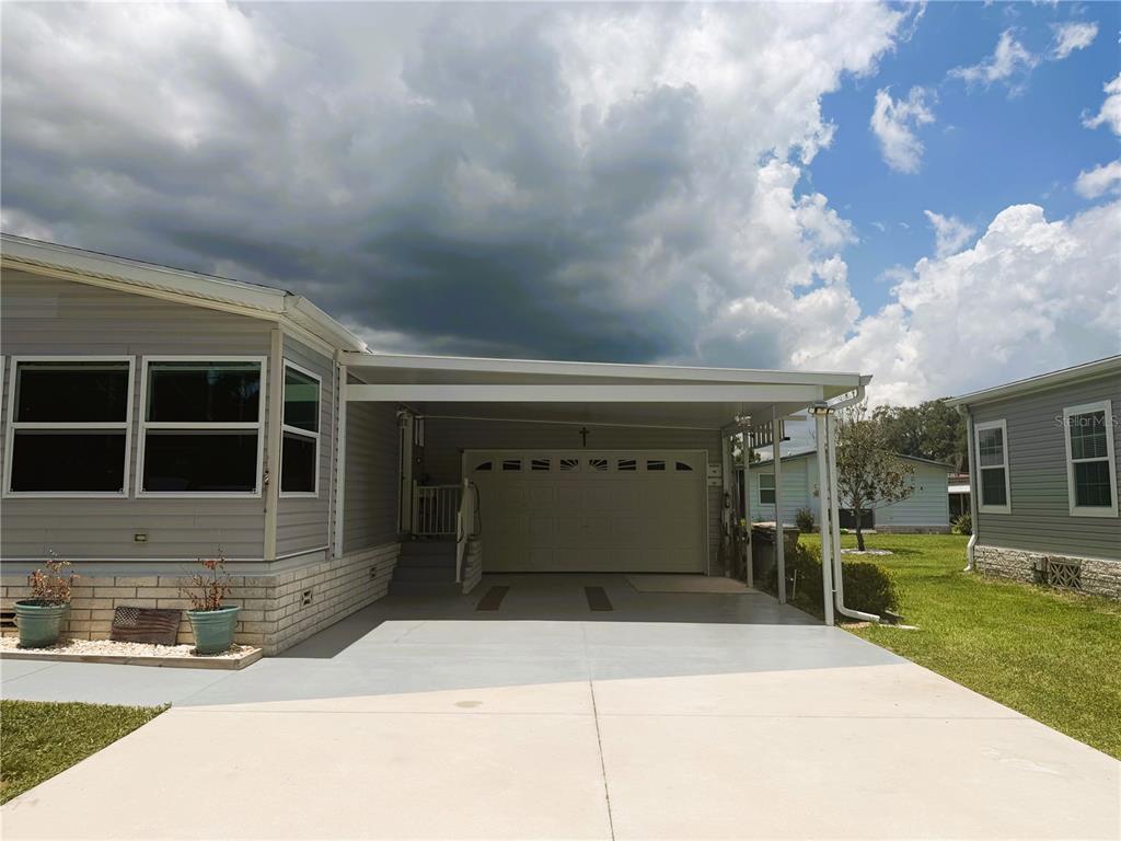 A gray manufactured home features a concrete driveway, a covered carport, and a garage door — 165 SAGO PALM DRIVE, LEESBURG, FL
