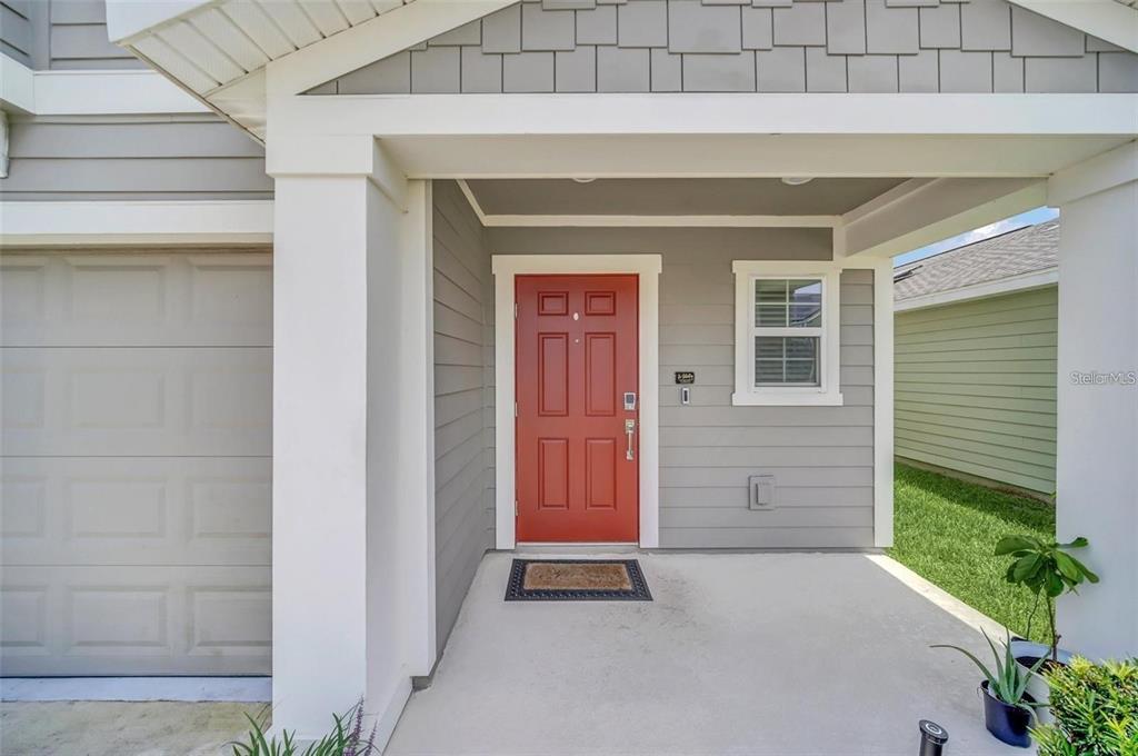 A covered front porch features a red door, gray siding, and a concrete floor — 4382 SUNNY CREEK PL, KISSIMMEE, FL