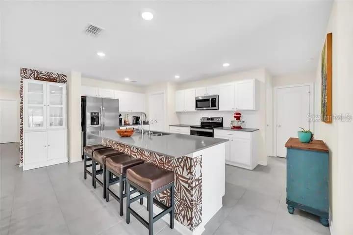 A modern kitchen features white cabinetry, stainless steel appliances, and a central island with seating — 4382 SUNNY CREEK PL, KISSIMMEE, FL