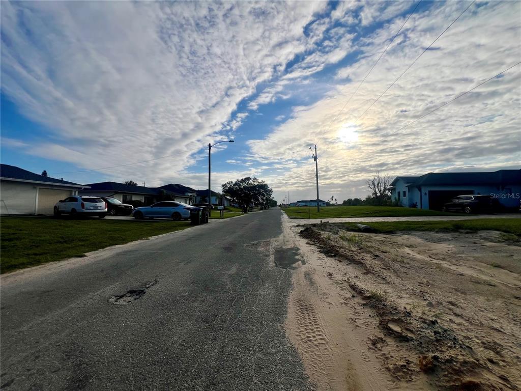 A paved residential street with houses, parked cars, and a sandy shoulder under a cloudy sky — 934 NE 12TH STREET, CAPE CORAL, FL
