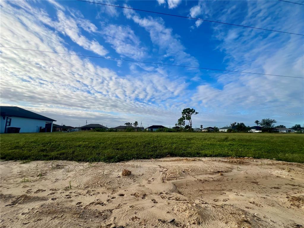A wide, grassy vacant lot sits under a blue sky with scattered clouds — 934 NE 12TH STREET, CAPE CORAL, FL