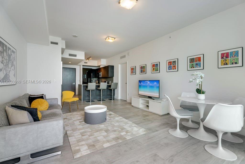An open-concept living and dining area features light wood flooring, a grey sofa, and kitchen — 1080 Brickell Ave # 3602, Miami FL 33131, MIAMI, FL