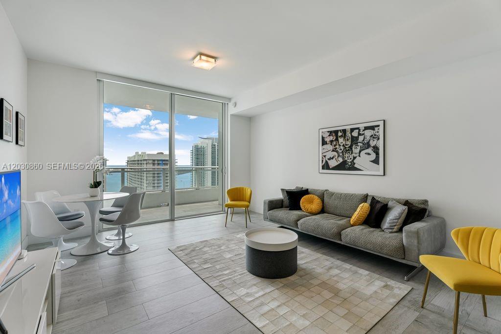 A living room features a grey sofa, yellow accent chairs, and a view of the ocean — 1080 Brickell Ave # 3602, Miami FL 33131, MIAMI, FL