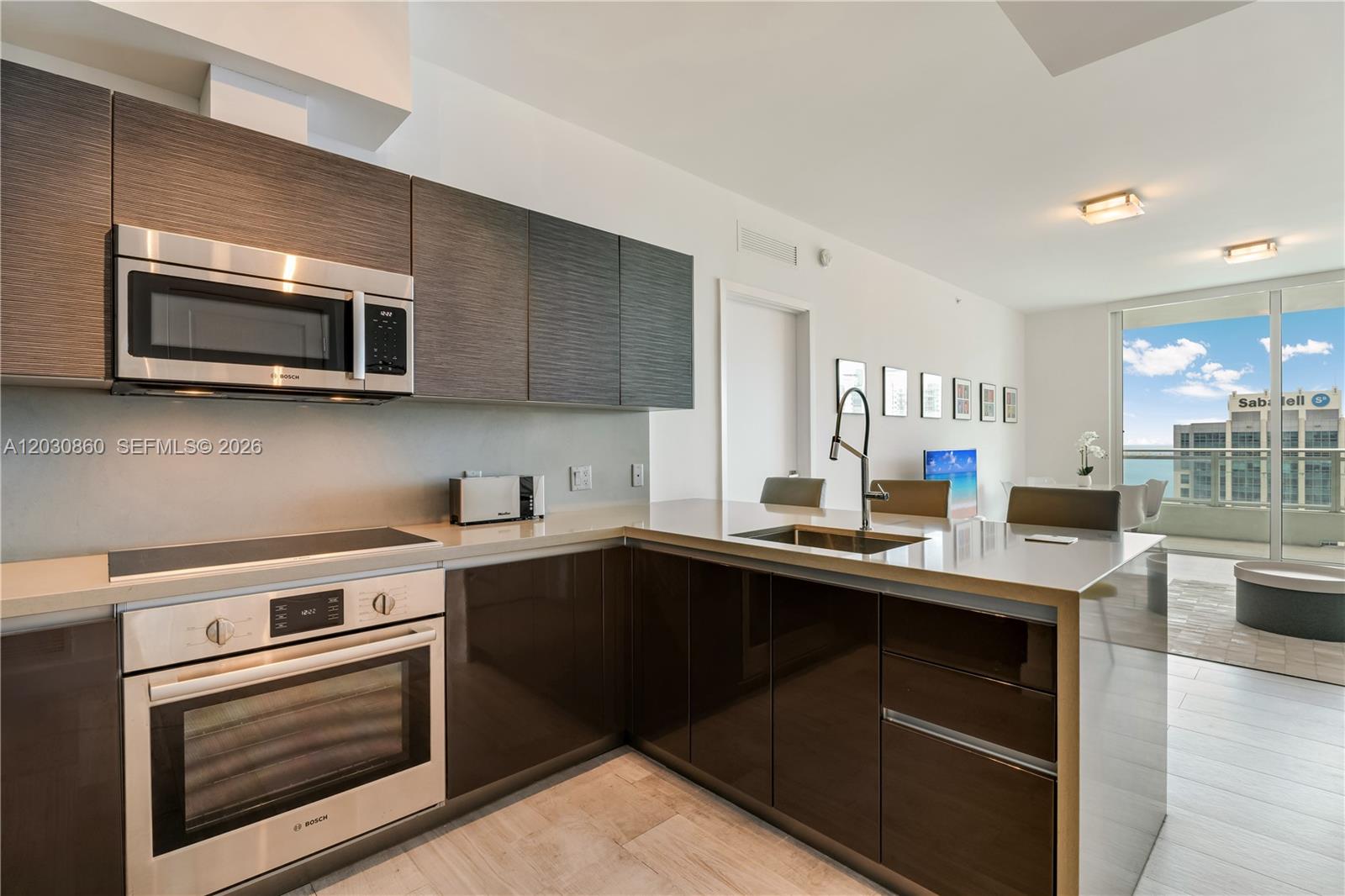 A modern kitchen features dark cabinetry, stainless steel appliances, and a view of the ocean — 1080 Brickell Ave # 3602, Miami FL 33131, MIAMI, FL