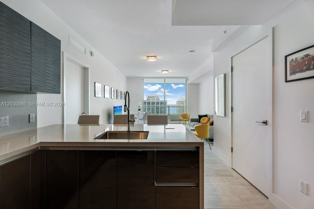 A modern kitchen with dark cabinetry overlooks a living area with floor-to-ceiling windows — 1080 Brickell Ave # 3602, Miami FL 33131, MIAMI, FL