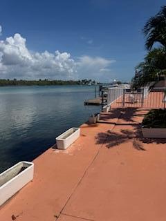 A concrete patio overlooks a calm waterway with a small wooden dock and palm trees — 225 S Beach Road Unit 205, Jupiter FL 33469, JUPITER, FL