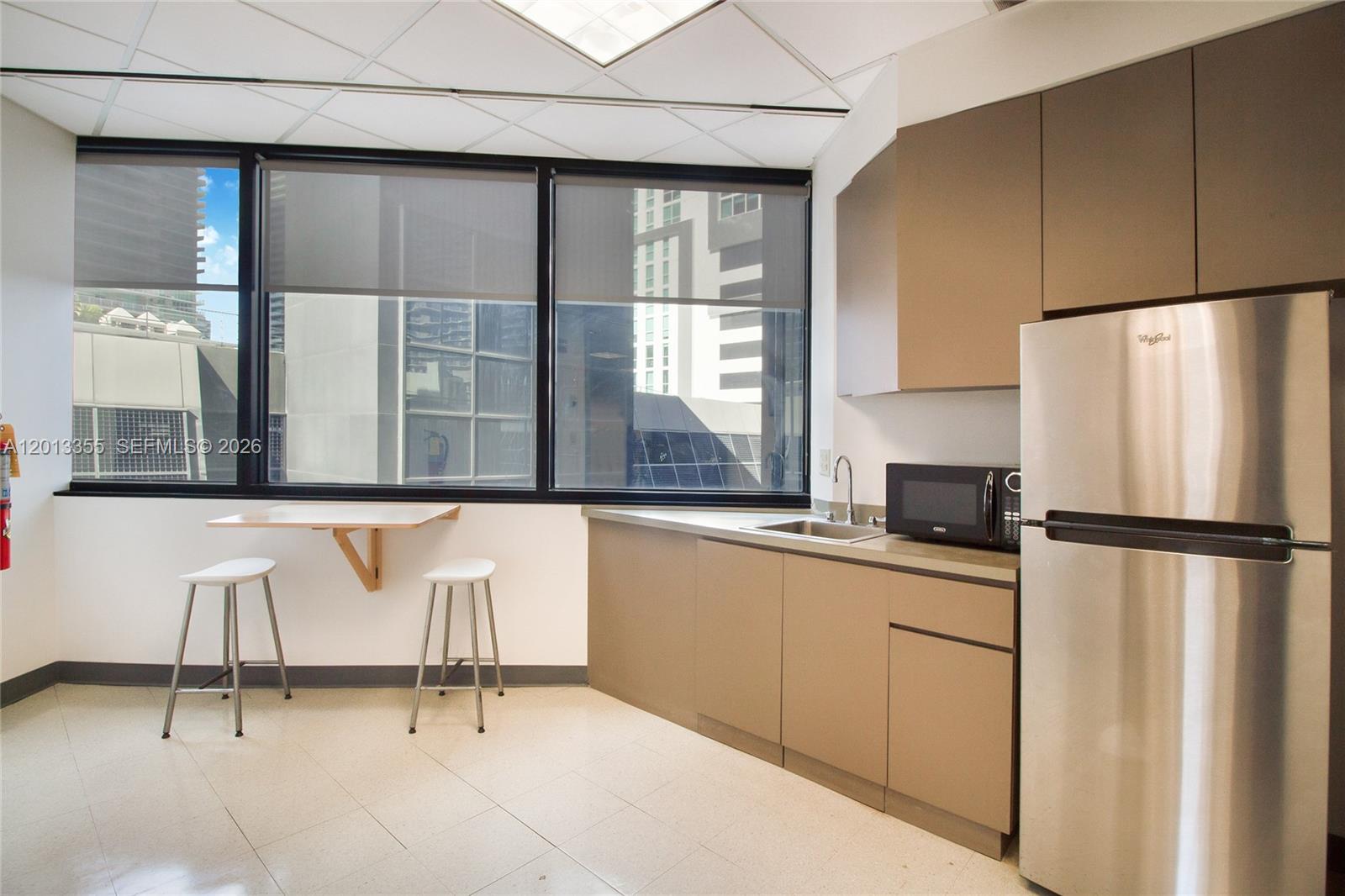 A small office kitchenette features a stainless steel refrigerator, sink, microwave, and wall-mounted table — 1200 Brickell Ave # B, Miami FL 33131, MIAMI, FL