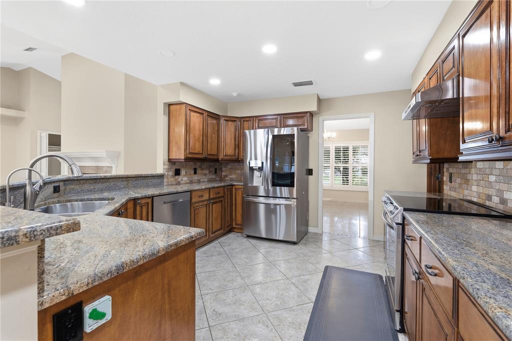 A kitchen features wood cabinets, granite countertops, stainless steel appliances, and light-colored tile flooring — 1889 BERKELEY COURT, MAITLAND, FL
