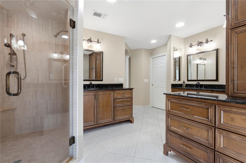 A bathroom features a glass-enclosed shower, dual wood vanities with dark countertops, and tile flooring — 1889 BERKELEY COURT, MAITLAND, FL