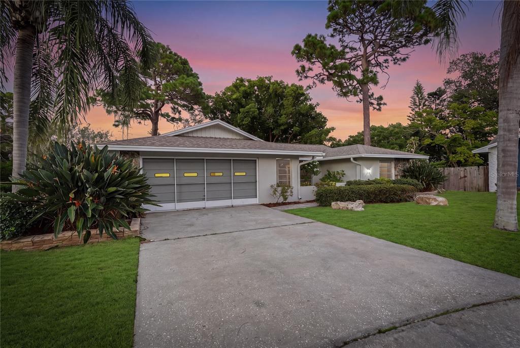 A single-story house with a gray garage door, concrete driveway, and palm trees at sunset — 505 BAMBOO COURT, TARPON SPRINGS, FL