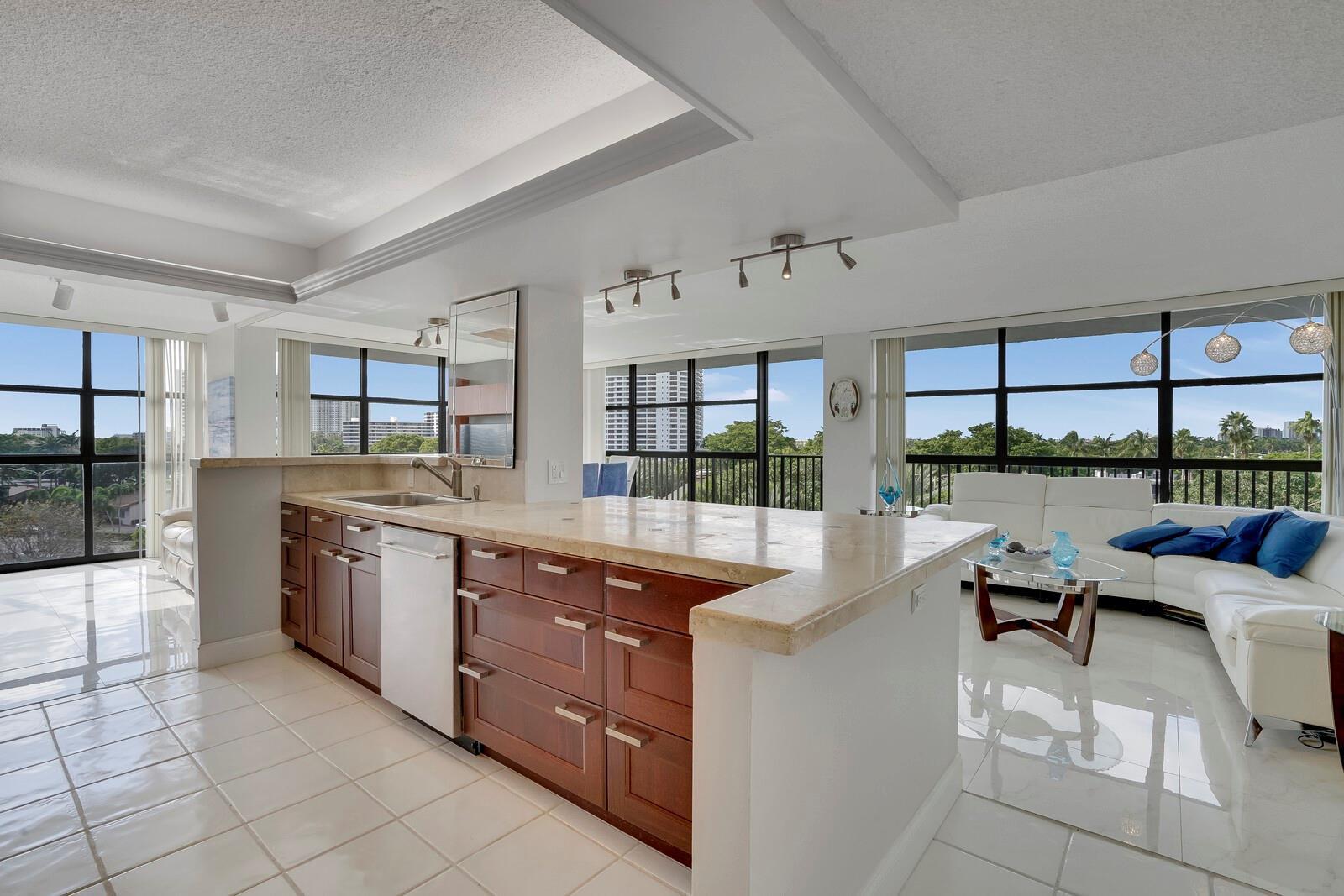 A kitchen with wood cabinets and stone countertops overlooks a living area with floor-to-ceiling windows — 600 Parkview Drive # 531, Hallandale Beach FL 33009, HALLANDALE BEACH, FL