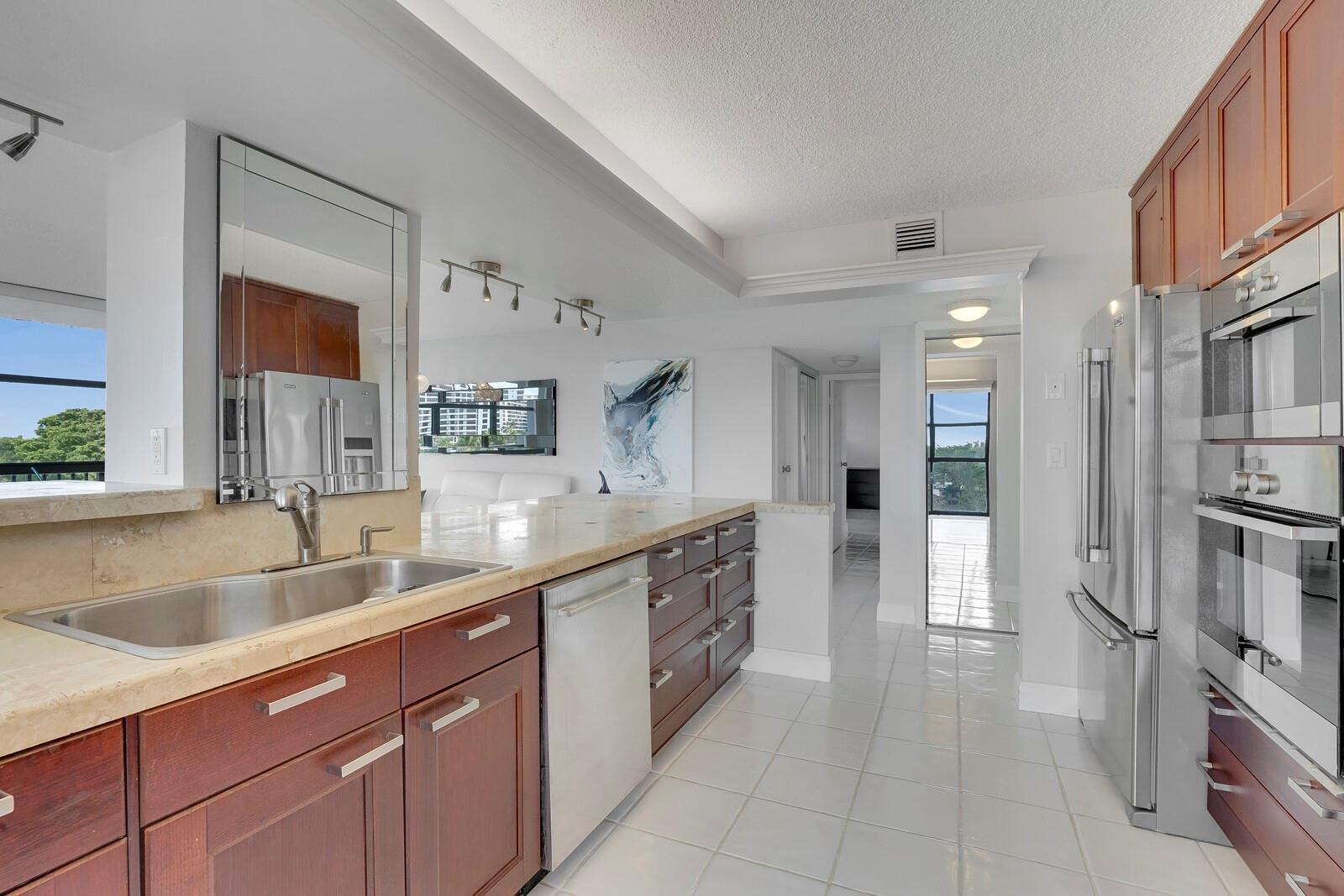A kitchen features dark wood cabinets, stainless steel appliances, and light-colored countertops and tile floors — 600 Parkview Drive # 531, Hallandale Beach FL 33009, HALLANDALE BEACH, FL