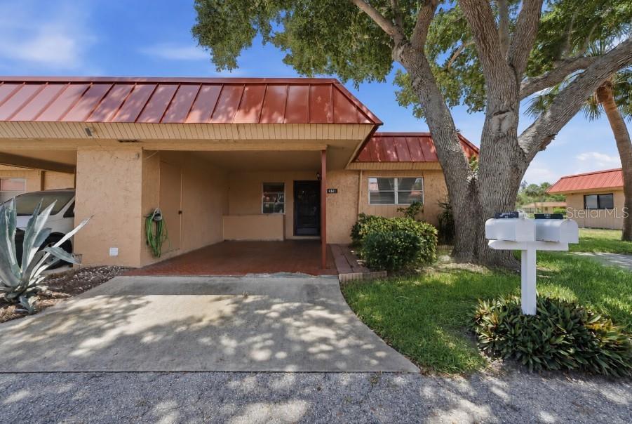 A single-story residence features a covered carport, a reddish-brown metal roof, and a large tree — 4111 LA COSTA COVE UNIT 4111, BRADENTON, FL