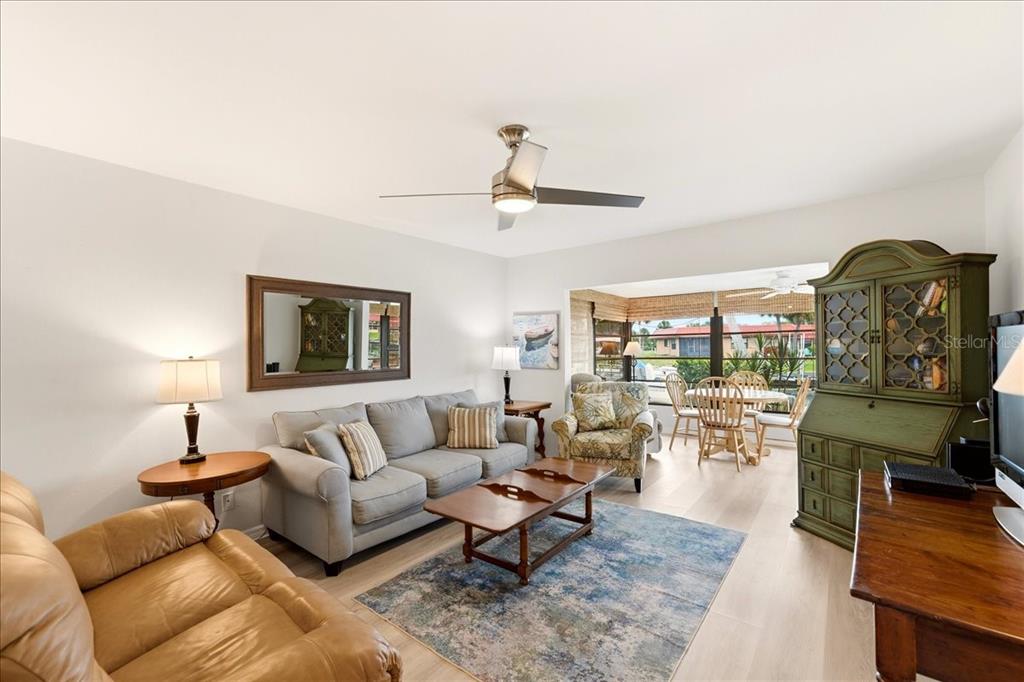 A living room with a grey sofa, leather chair, green hutch, and a sunroom beyond — 4111 LA COSTA COVE UNIT 4111, BRADENTON, FL