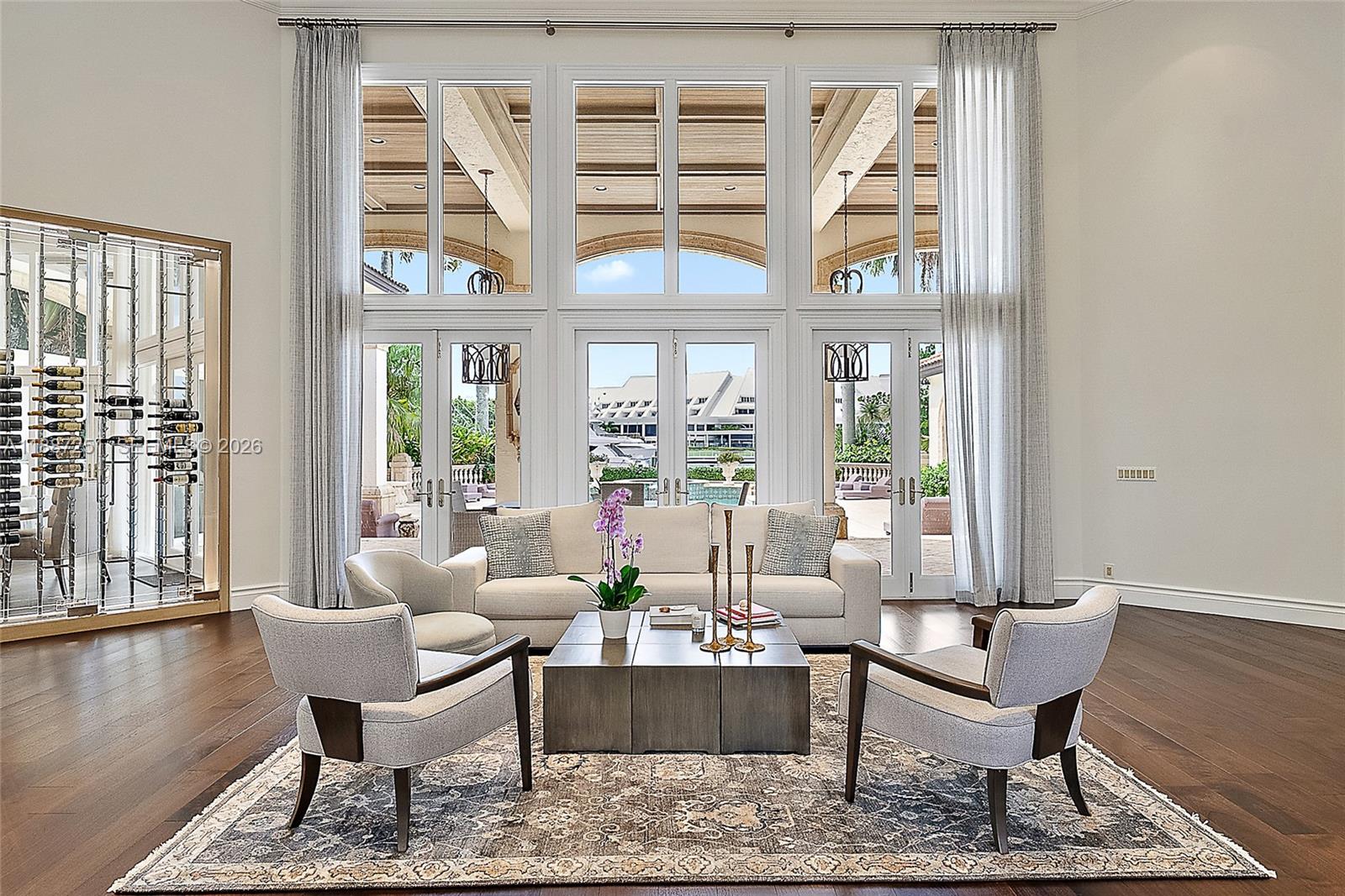A living room features a large wine display, floor-to-ceiling windows, and a view of a pool — 193 Spyglass Ct, Jupiter FL 33477, JUPITER, FL