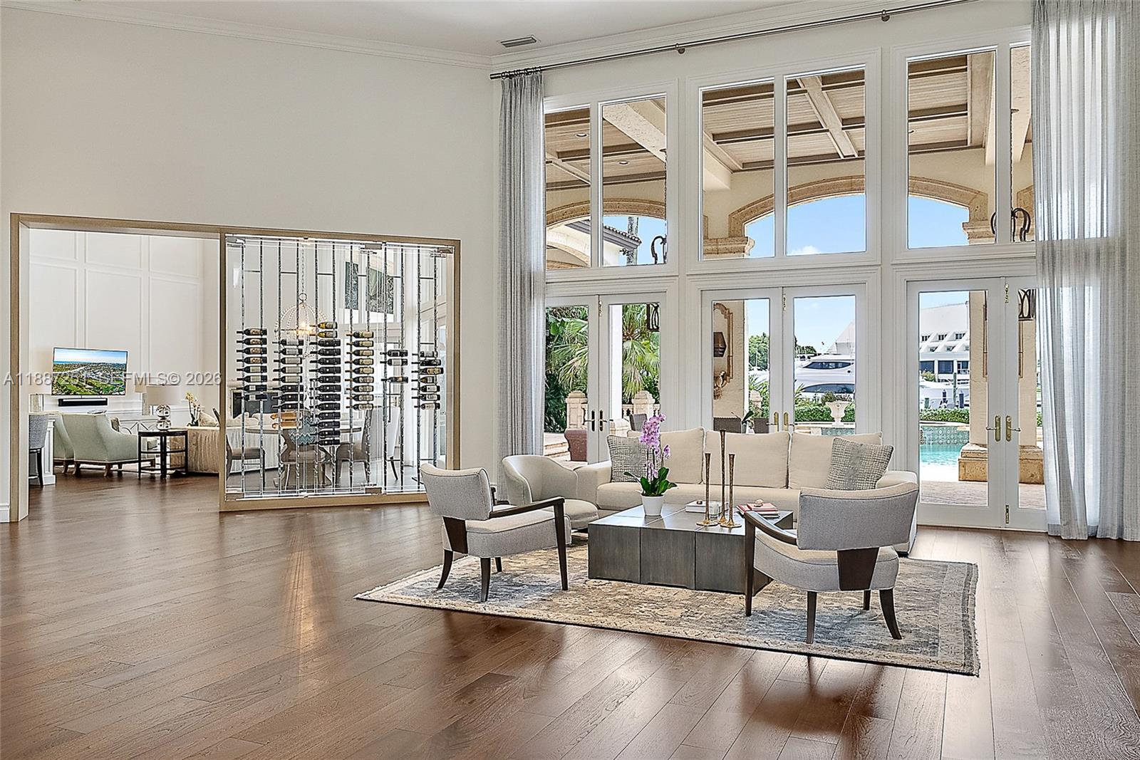 A spacious living room features a glass-enclosed wine cellar, high ceilings, and floor-to-ceiling windows — 193 Spyglass Ct, Jupiter FL 33477, JUPITER, FL