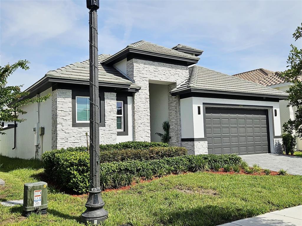 A single-story house features a stone facade, a gray garage door, and a tiled roof — 260 HAMPTON LOOP, DAVENPORT, FL