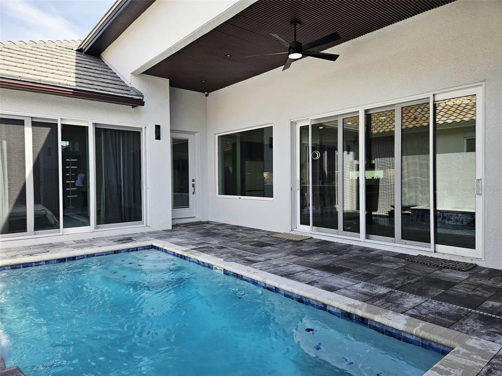 A swimming pool sits on a stone patio outside a house with sliding glass doors — 260 HAMPTON LOOP, DAVENPORT, FL