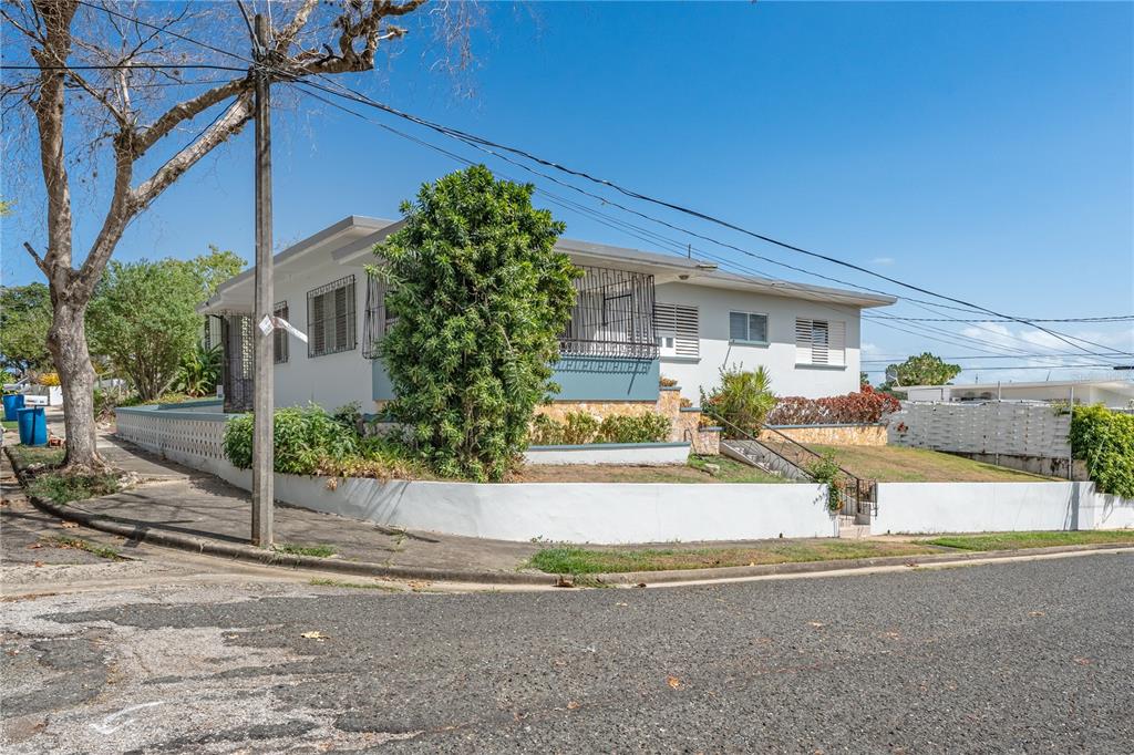 A corner lot features a light-colored single-story house with a white retaining wall and landscaping — 69 Urbanizacion Ramirez SAGRADO CORAZON ST UNIT 69, CABO ROJO, PR