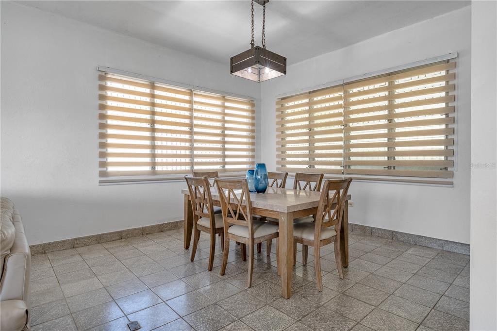 A dining room features a stone-topped table, wooden chairs, tile flooring, and zebra-style window blinds — 69 Urbanizacion Ramirez SAGRADO CORAZON ST UNIT 69, CABO ROJO, PR