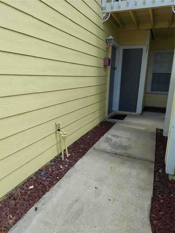 A yellow-sided building exterior features a concrete walkway, a gray door, and a water spigot — 2027 ROYAL BAY BOULEVARD UNIT 77, KISSIMMEE, FL
