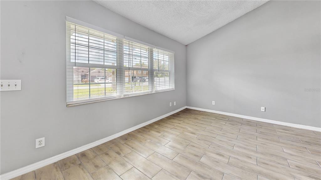 An empty room features light gray walls, wood-look tile flooring, and a large window — 305 MEDINA COURT, KISSIMMEE, FL