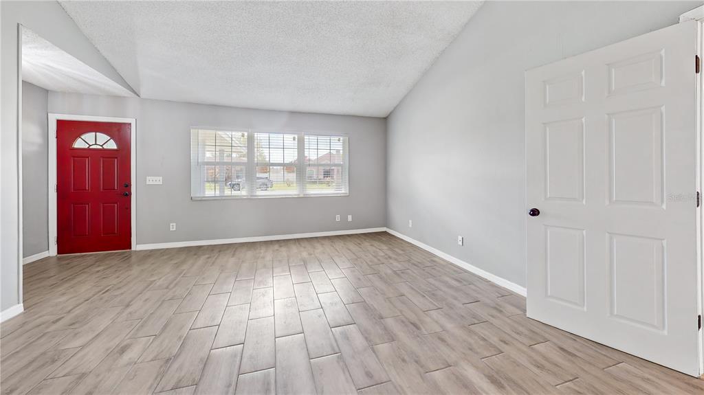 An empty room features light wood-look tile flooring, gray walls, a red door, and windows — 305 MEDINA COURT, KISSIMMEE, FL