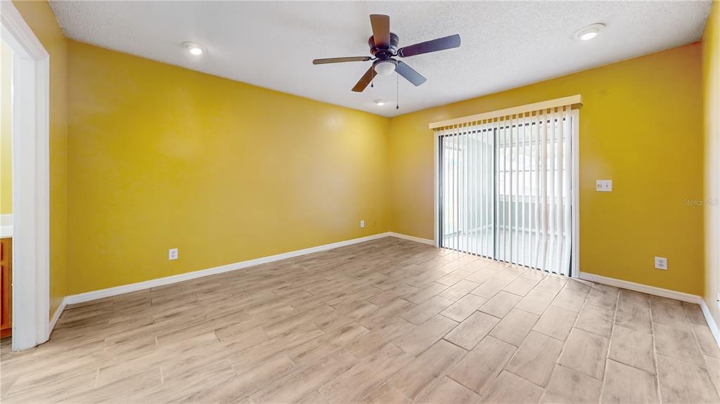An empty room with yellow walls, tile flooring, a ceiling fan, and sliding glass doors — 305 MEDINA COURT, KISSIMMEE, FL