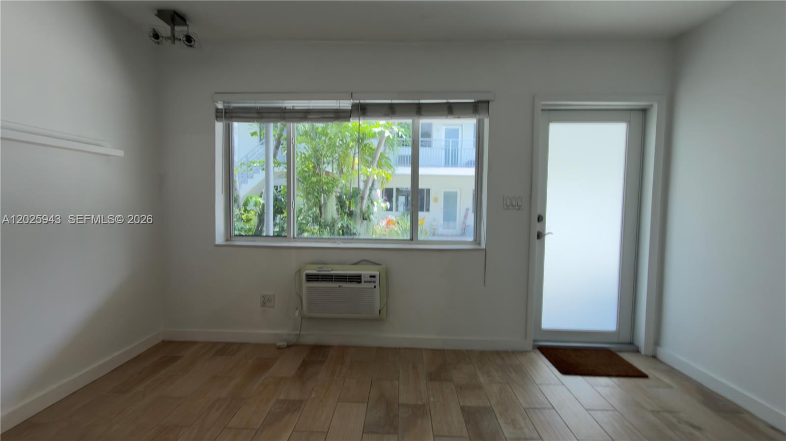 A room with light wood-look flooring, a window air conditioner, and a glass-paneled door — MIAMI BEACH, FL