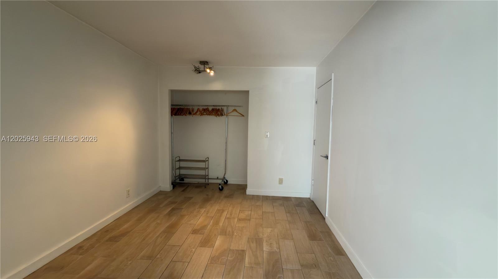 An empty room features light wood-look tile flooring, white walls, and an open closet area — MIAMI BEACH, FL