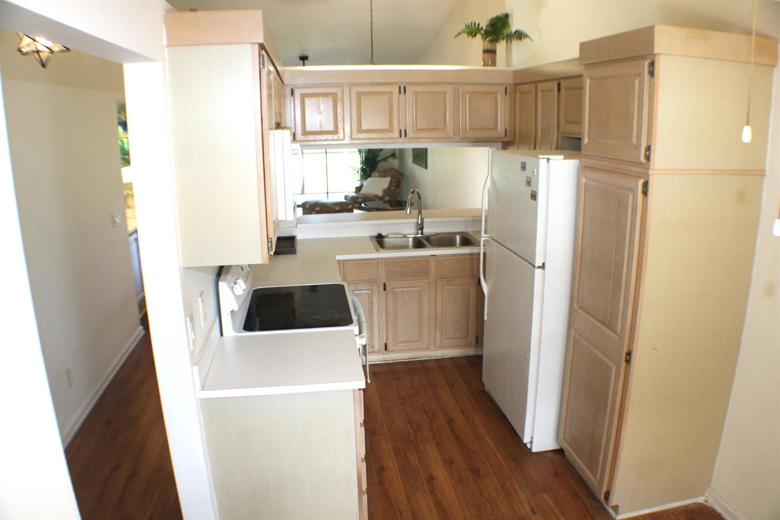 A galley kitchen features light wood cabinets, white appliances, and wood-look flooring — 1082 Keystone Drive # C, Jupiter FL 33458, JUPITER, FL
