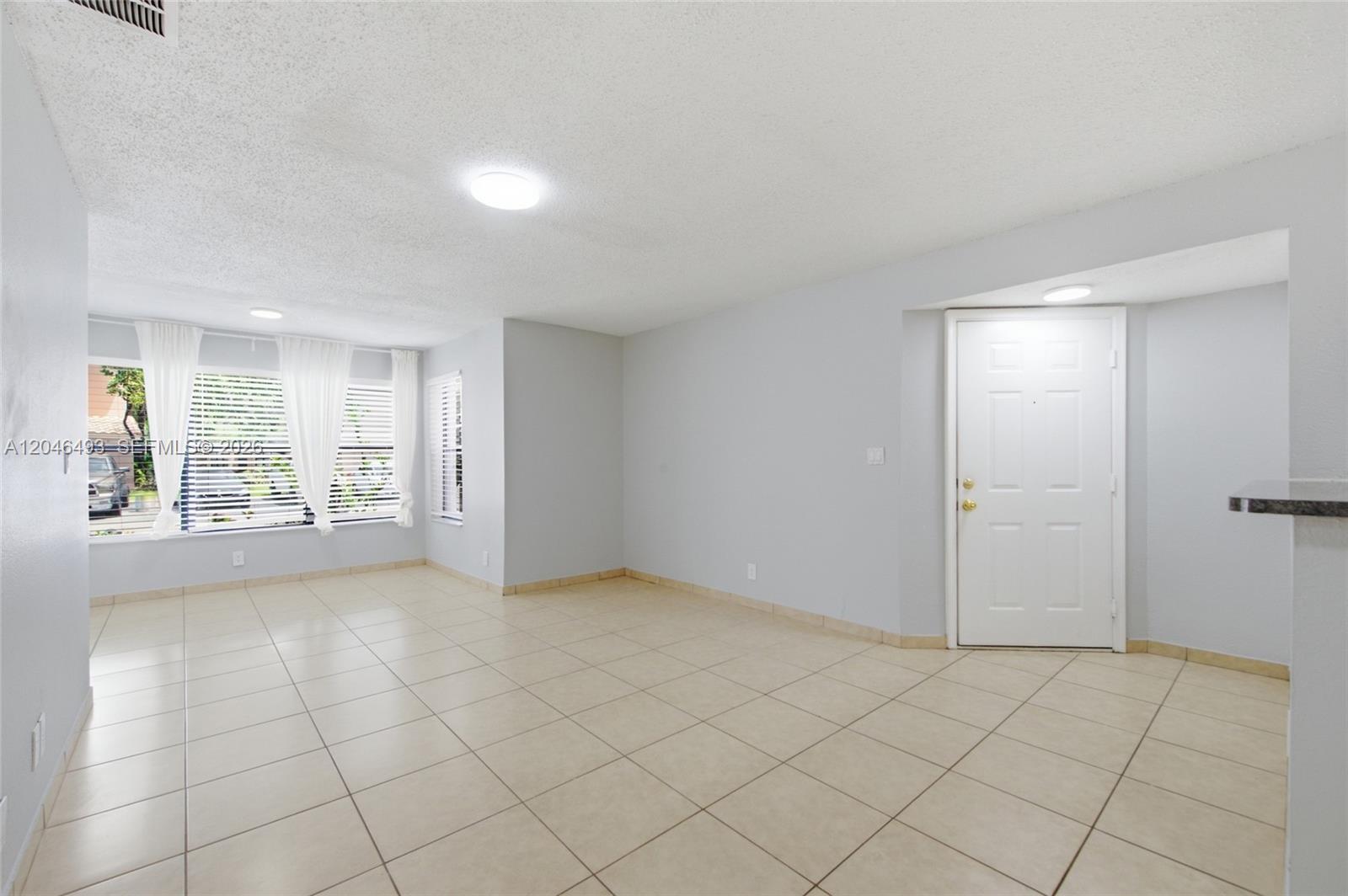 An empty living room features light-colored tile flooring, white walls, and a white entry door — 2846 S University Dr # 4104, Davie FL 33328, DAVIE, FL