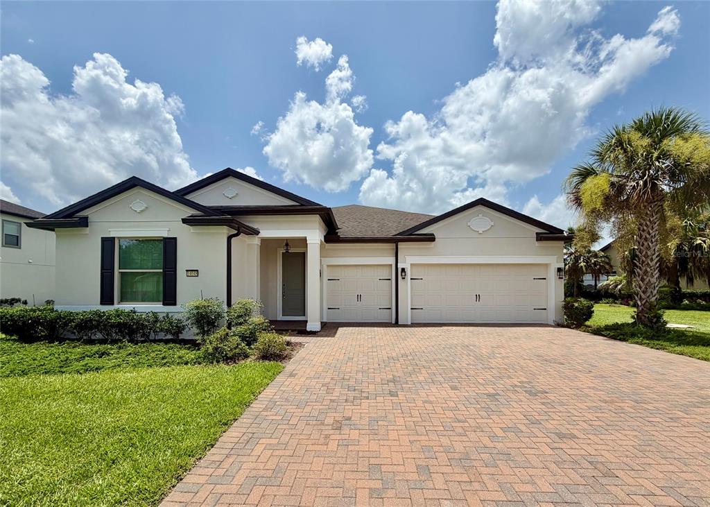 A single-story house with a beige stucco exterior, a brick paver driveway, and a three-car garage — 14048 LARKSPUR LAKE DRIVE, WINTER GARDEN, FL